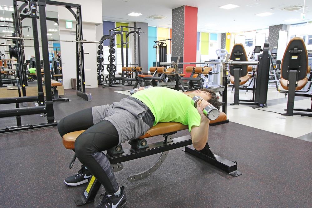 1. 両手にダンベルを持ち、膝に置いた状態でベンチに腰かける。ベンチに仰向けになり、胸の位置までダンベルを移動させます。